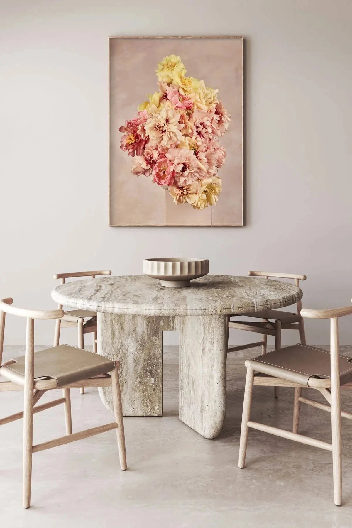 Fine art print of clustered pink and yellow peonies on soft blush background displayed above a sculptural marble dining table in an elegant neutral space
