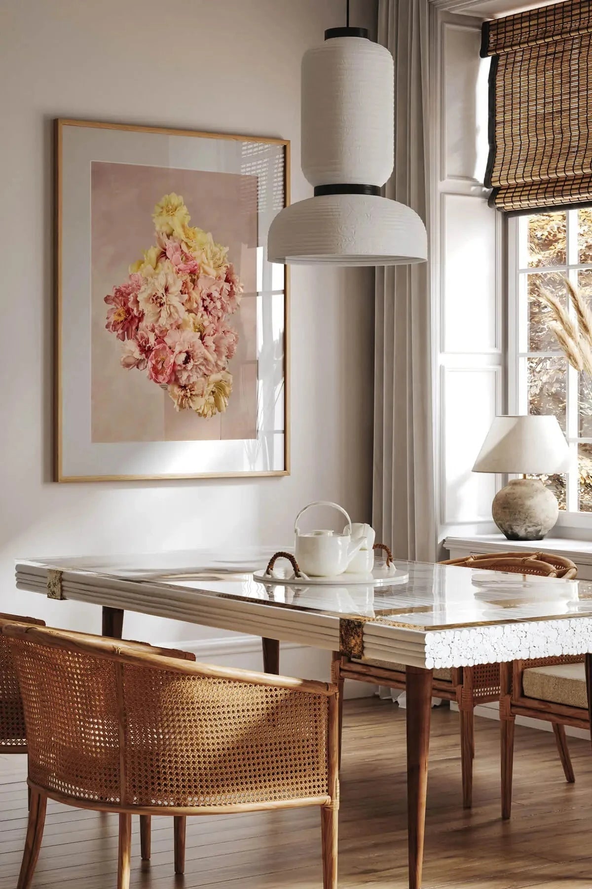 Fine art print of pink and yellow peonies arranged in a diamond shape on blush background, framed above marble dining table with cane chairs in sunlit room