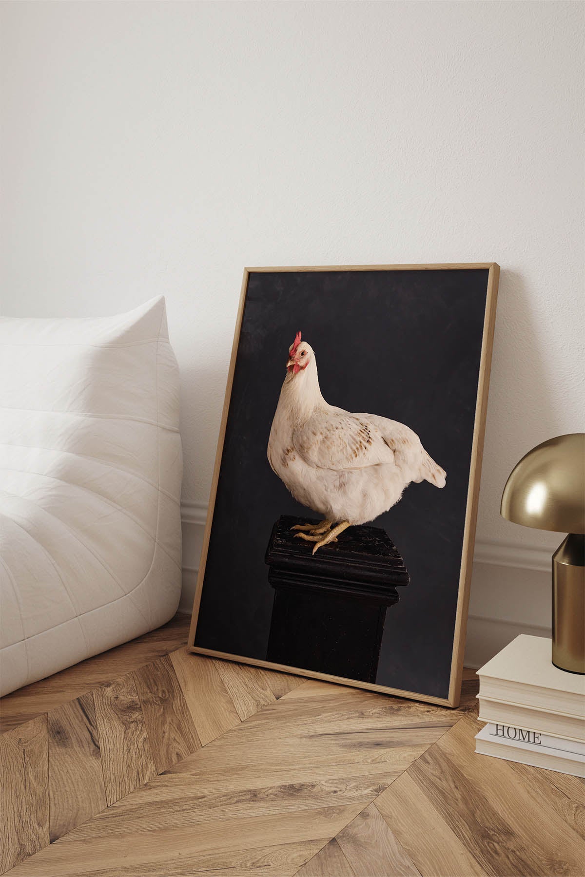 Fine Art Print Of A White Chicken Standing On A Black Plinth With A Black Background Framed Leaning Against A Wall Sitting On Oak Herringbone Floors.