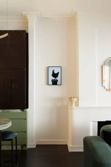 Fine art print of black rooster silhouette on white background displayed in elegant dining room with sage green chairs and white paneled walls