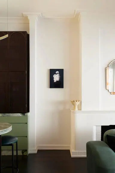 Fine art print of white peony bloom on black background displayed in elegant dining room with green velvet chairs and warm ambient lighting