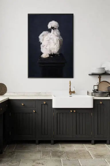 Fine art print of a fluffy white Silkie chicken perched on a black pedestal against a dark background, displayed above a black vanity with white basin in a modern bathroom.