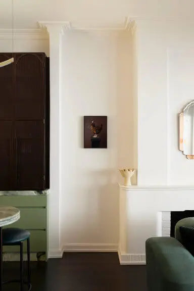 Fine art print of golden flowering branches on a dark burgundy background, displayed on a white wall between green velvet dining furniture in an elegant room