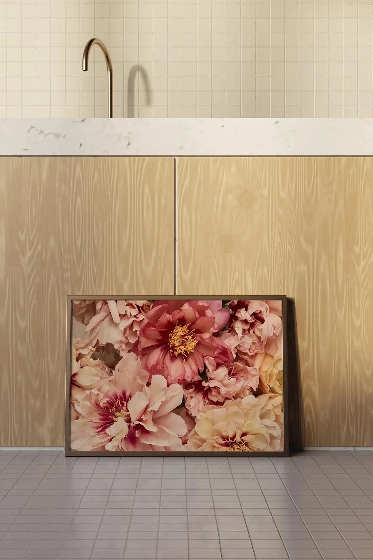 Fine art print of pink and blush peonies with golden centers leaning against light wood cabinetry beneath marble countertop and brass tapware