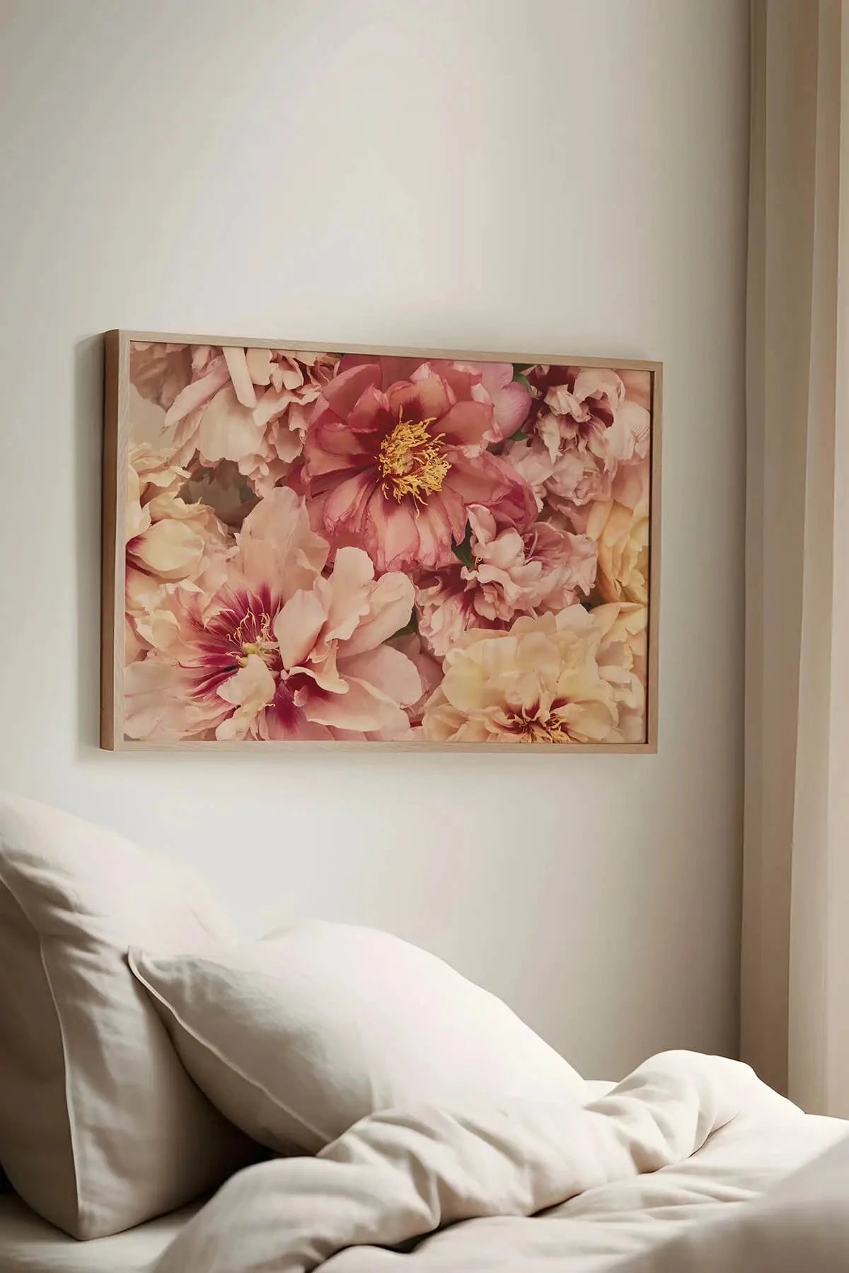 Canvas wall hanging of soft pink and coral peonies with golden centers in a lush floral arrangement, displayed above white bedding in a serene bedroom.