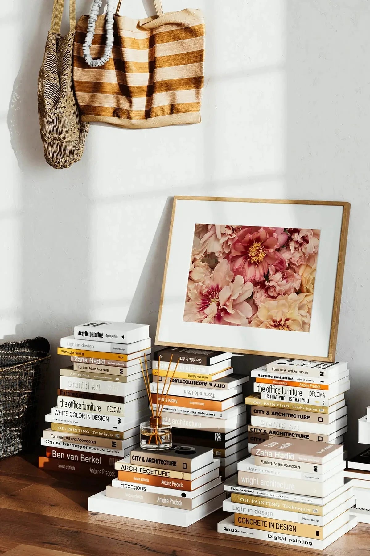 Fine art print of lush peony blooms in soft pink and mauve tones displayed in timber frame on stacked design books beside a reed diffuser