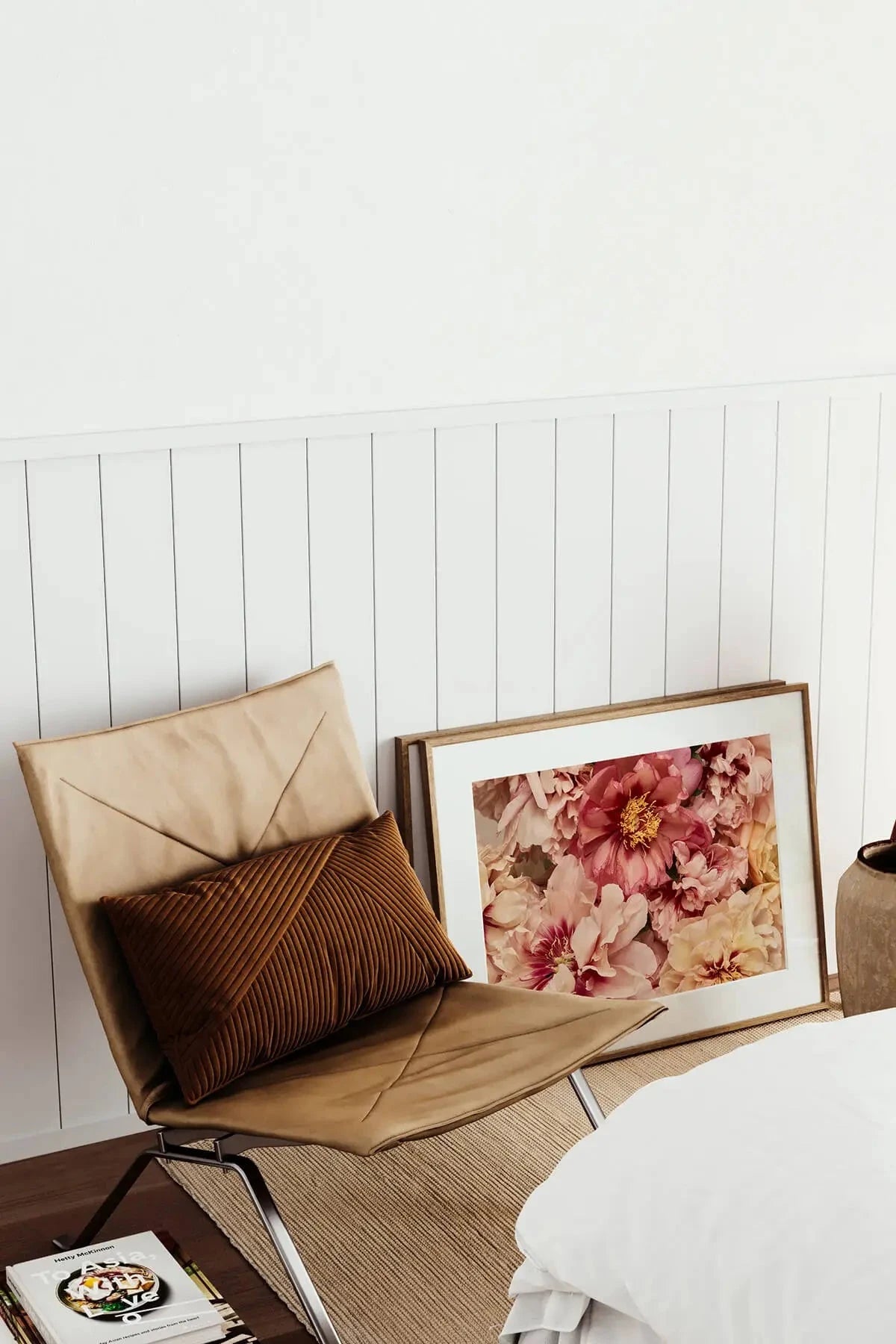 Fine art print of blush pink and coral peonies with golden yellow centers leaning against a tan leather chair in a bright modern interior