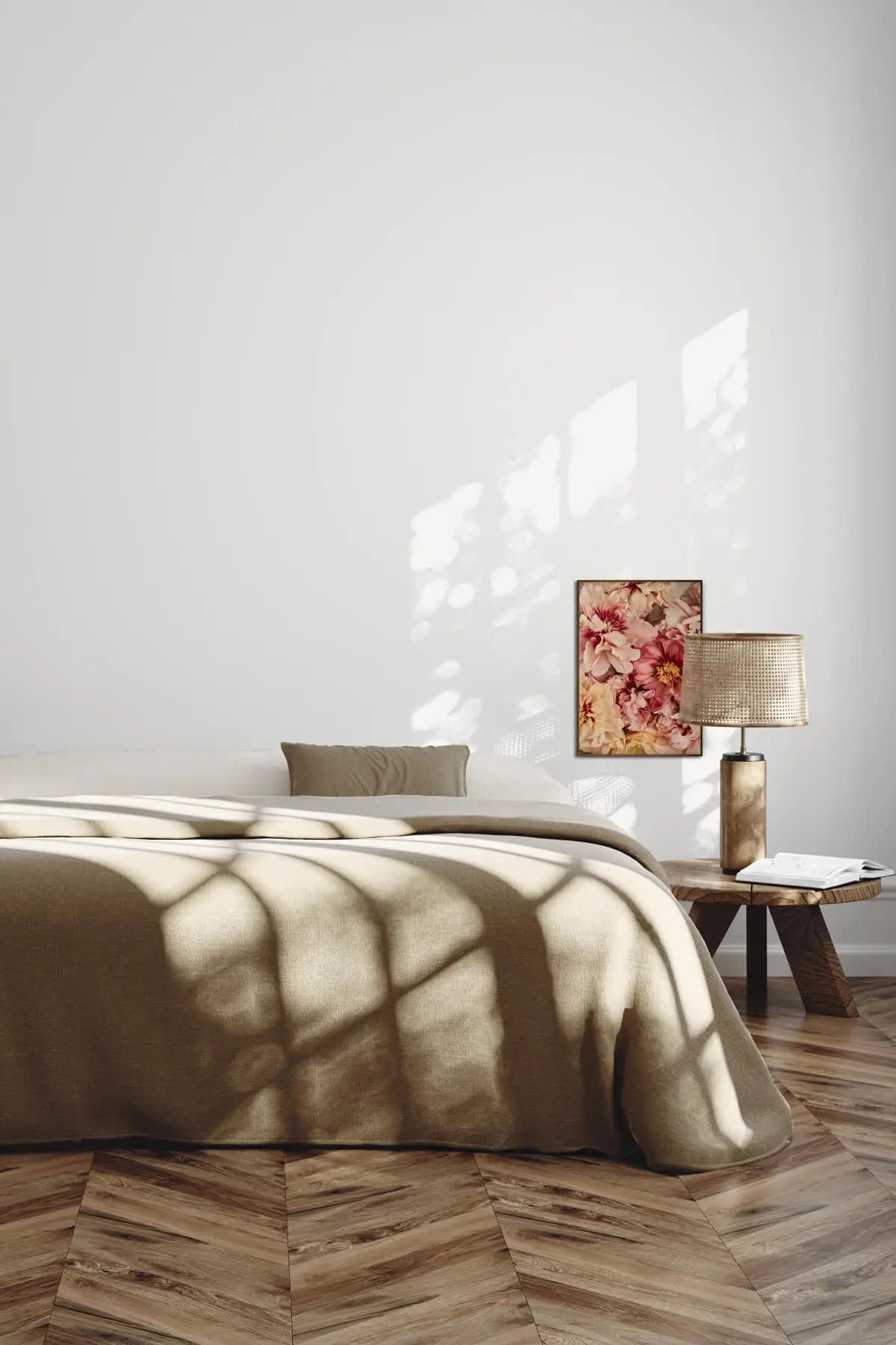 Fine art print of soft pink and burgundy peonies hung above a bed with olive linen in a sunlit minimalist bedroom.