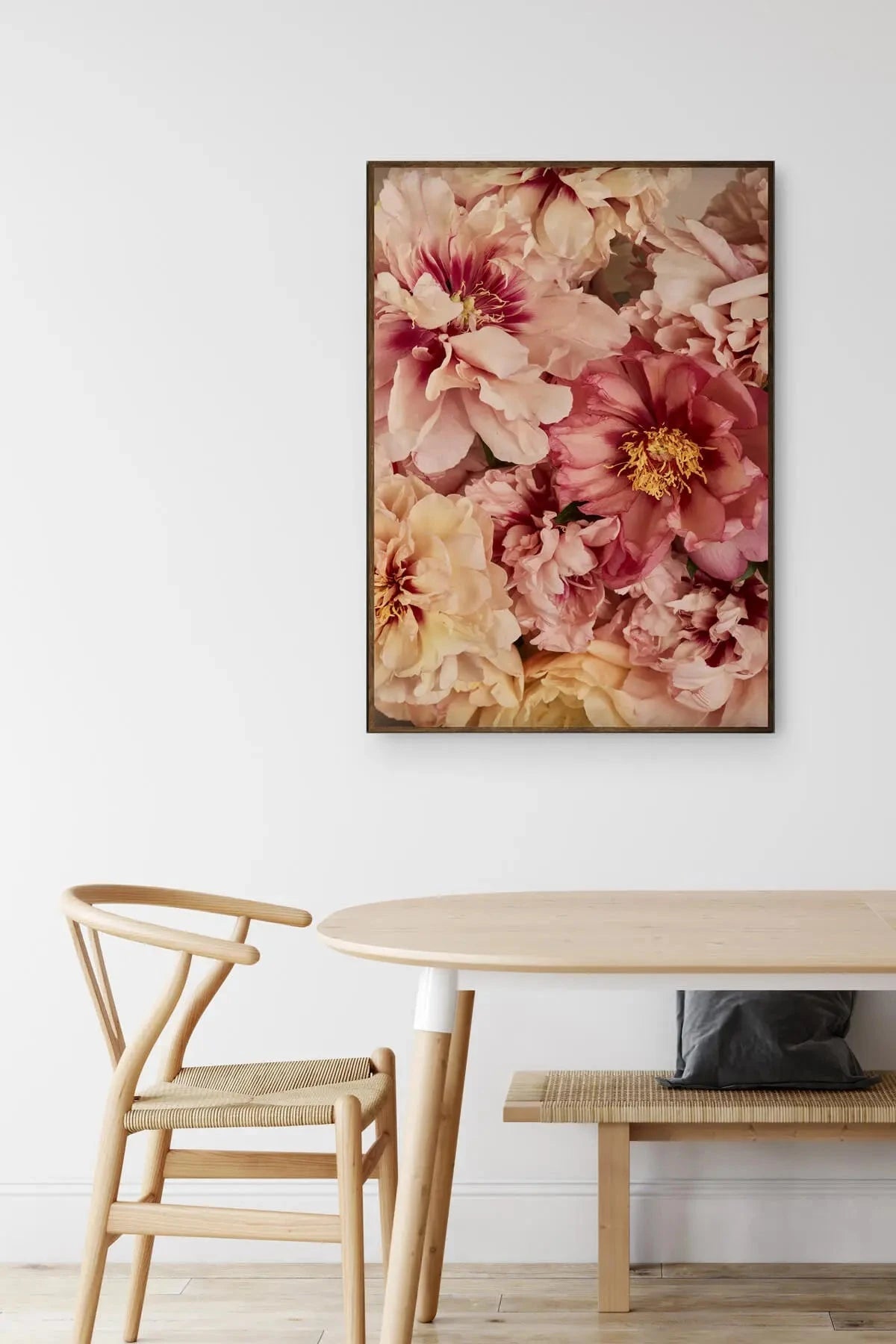 Fine art print of lush blush and cream peonies with golden stamens displayed above a natural timber dining table and wishbone chair