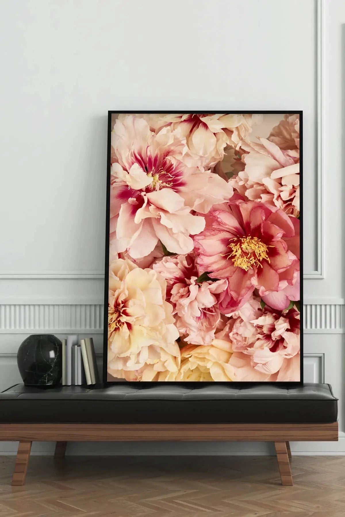 Fine art print of lush peonies in soft pink, cream and yellow tones with golden stamens, displayed in black frame on modern console table against white panelled wall