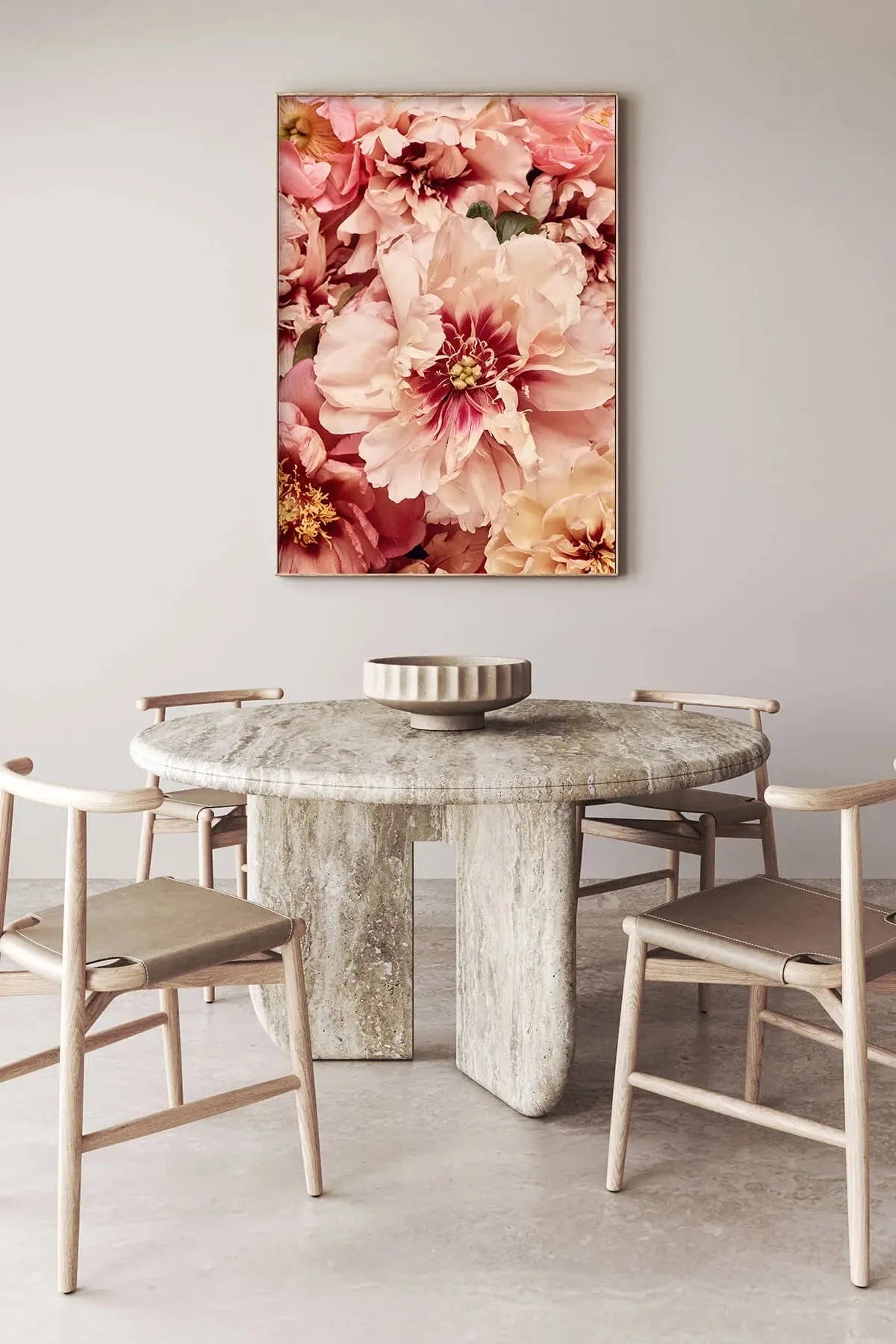 Fine art print of soft pink and coral peonies with deep burgundy centers displayed above a modern travertine dining table in an elegant neutral dining room