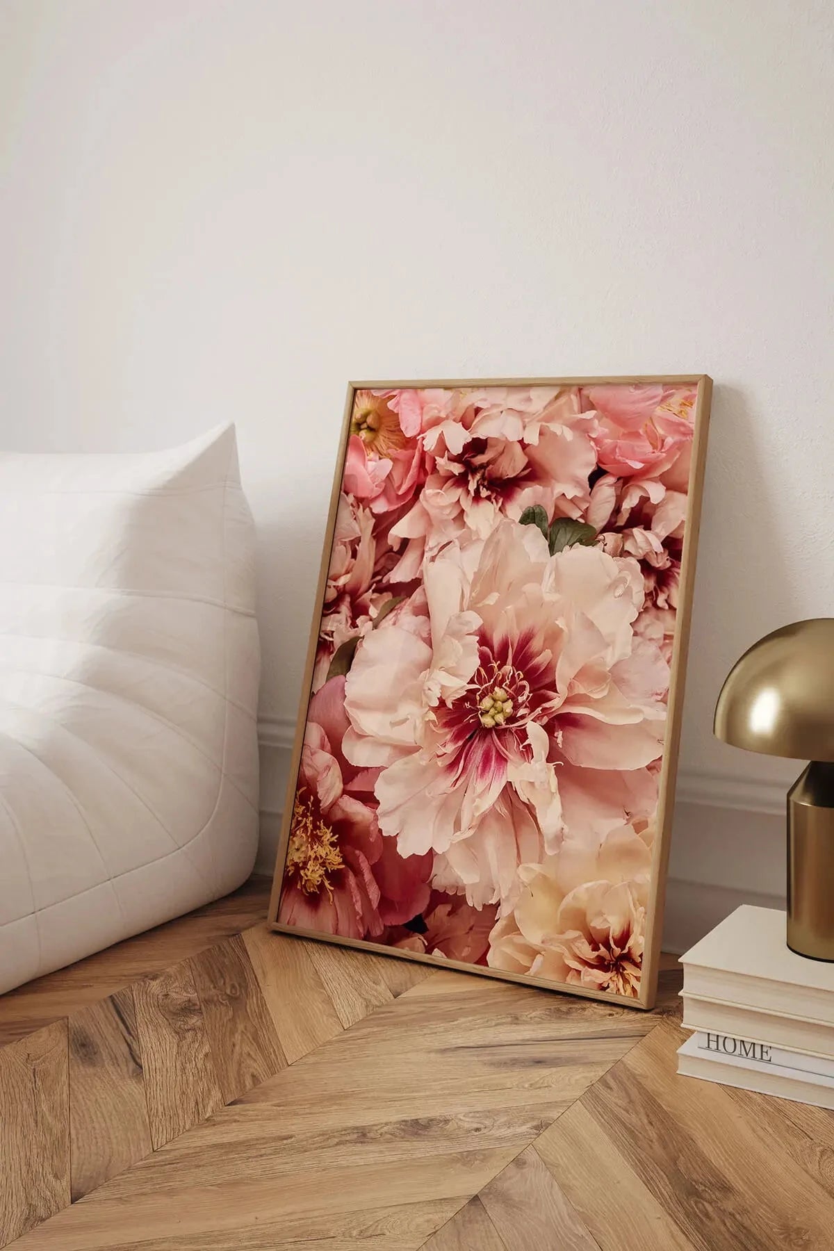 Fine art print of layered blush pink and coral peonies in full bloom leaning against white bedding on herringbone timber floors