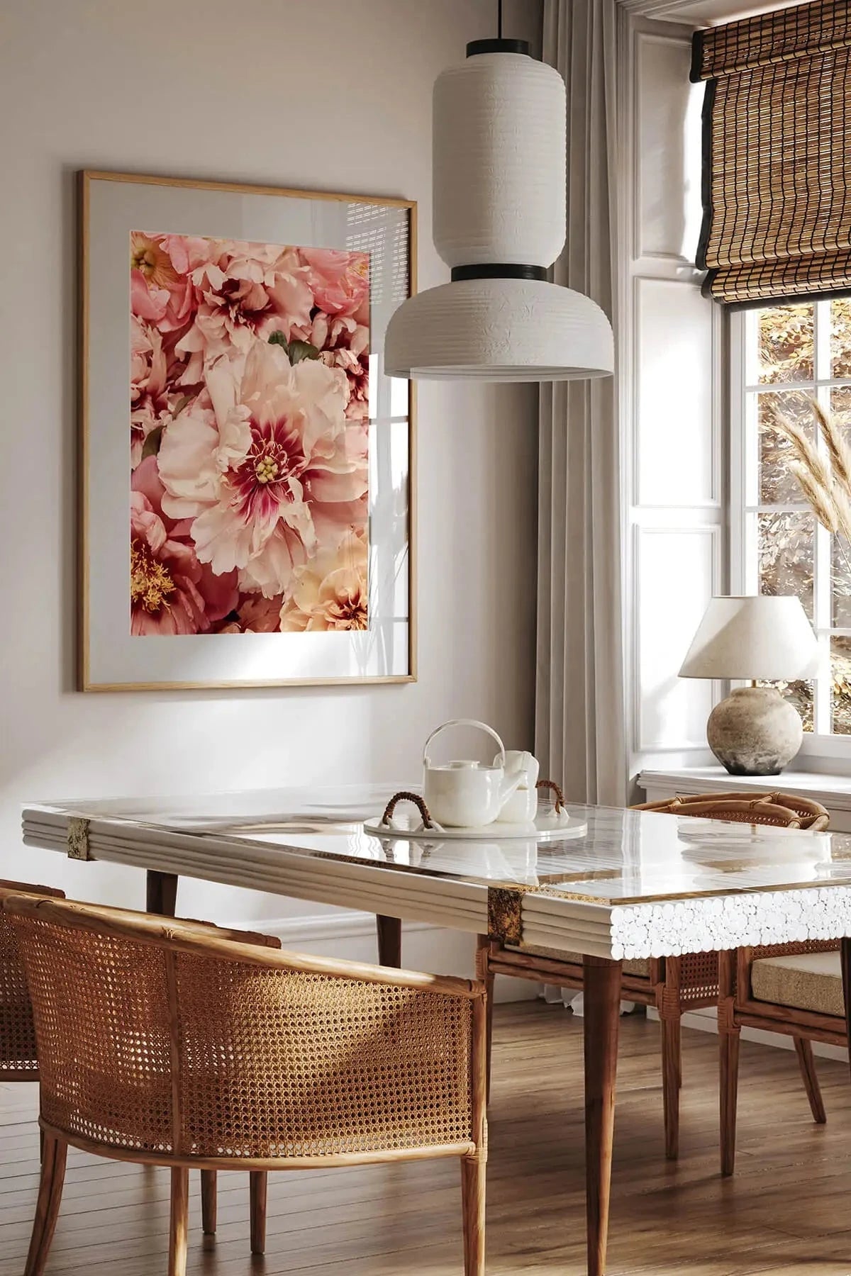 Fine art print of lush pink and coral peonies in full bloom displayed above a dining table with cane chairs and pendant lighting in a sunlit room