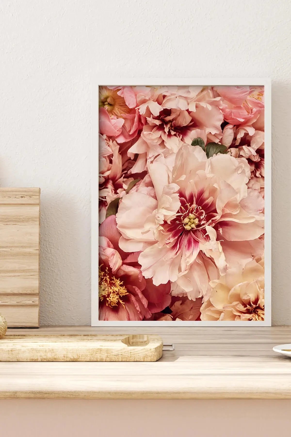 Fine art print of soft pink and blush peonies with burgundy centers displayed on a white shelf with wooden cutting boards