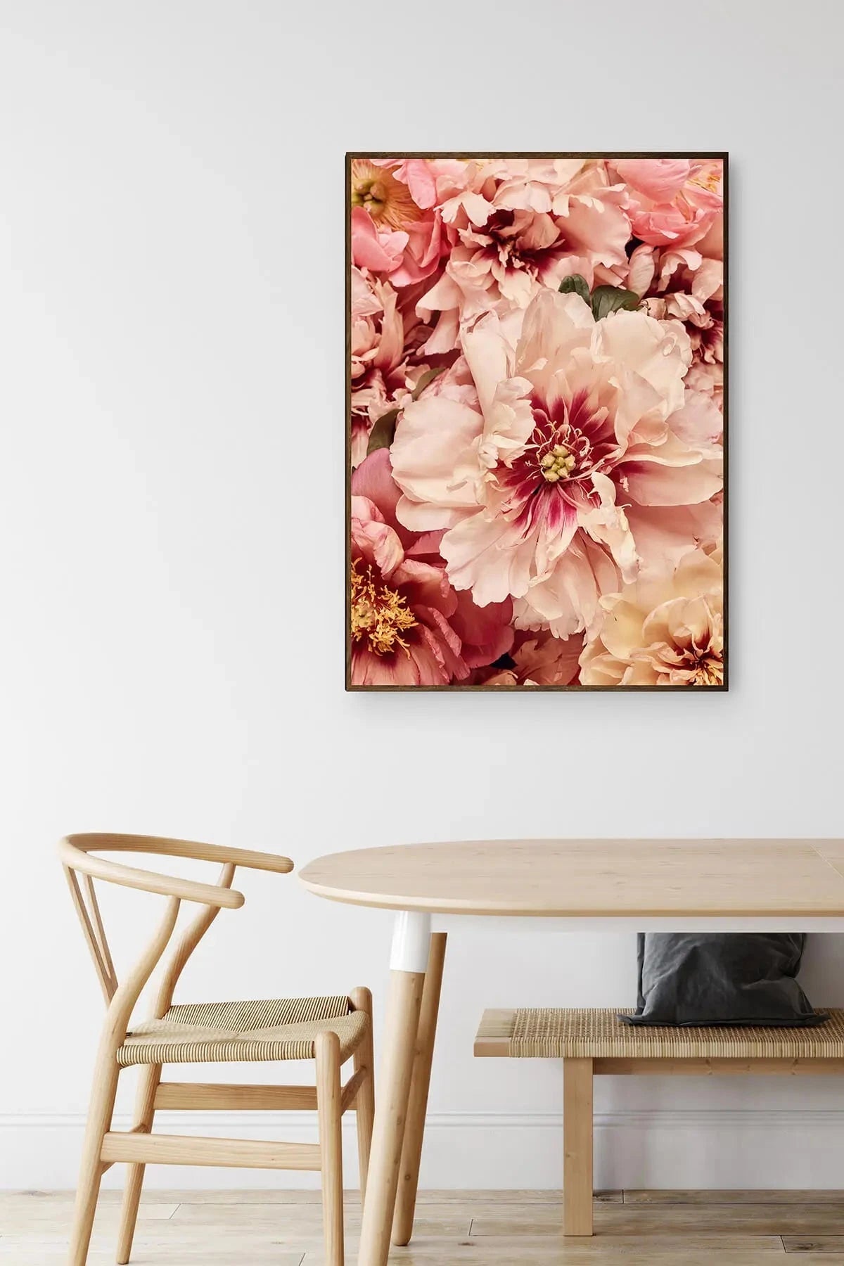 Fine art print of lush pink and blush peonies with burgundy centers displayed above a natural timber dining table with wishbone chair.