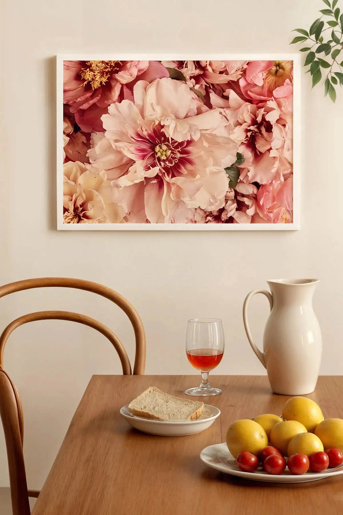 Fine art print of blush pink and cream peonies with golden stamens hanging above a dining table set with fresh fruit and rosé wine