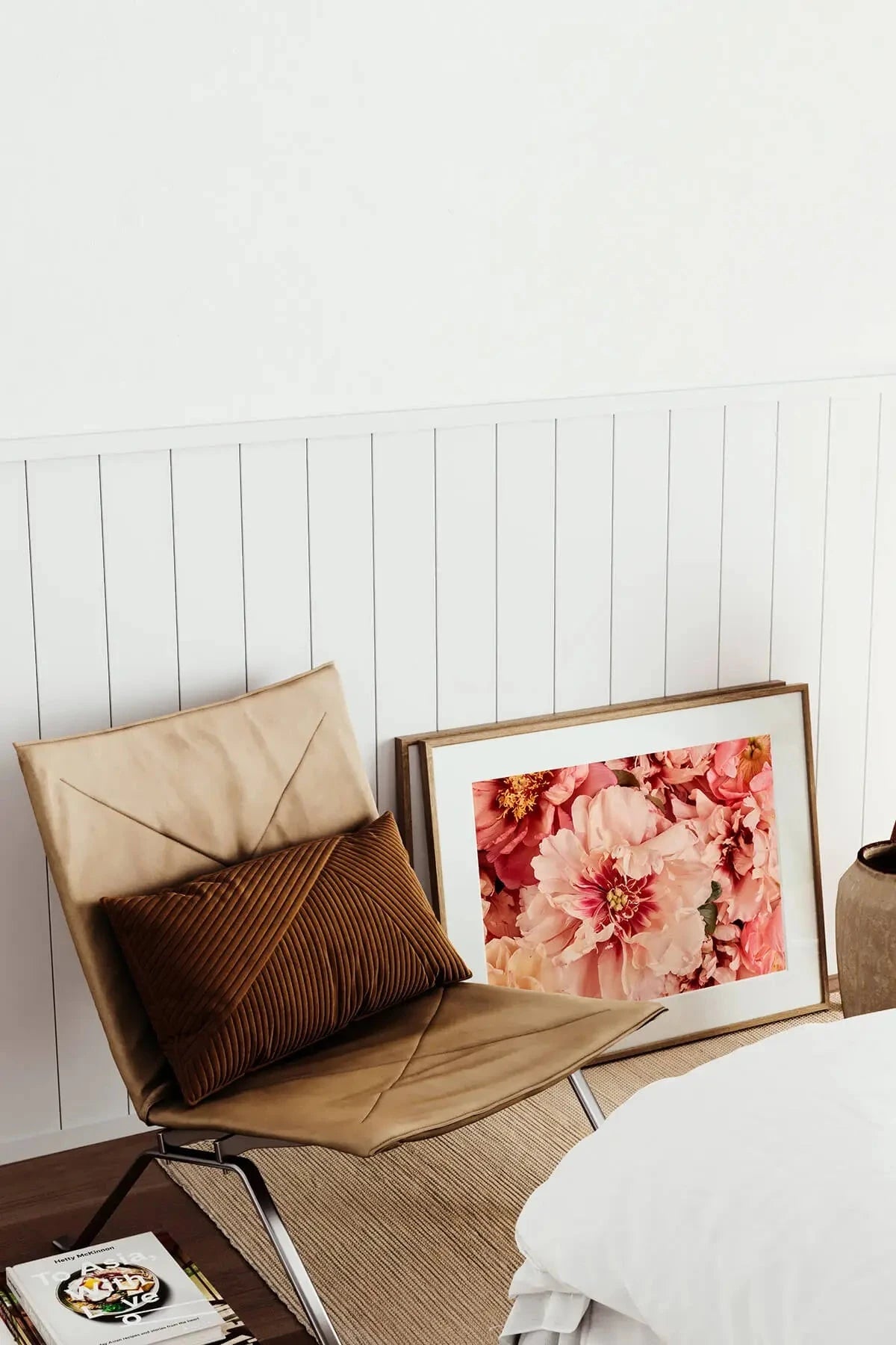 Fine art print of lush pink and coral peonies with golden centers leaning against white paneling beside a tan leather chair with cushions