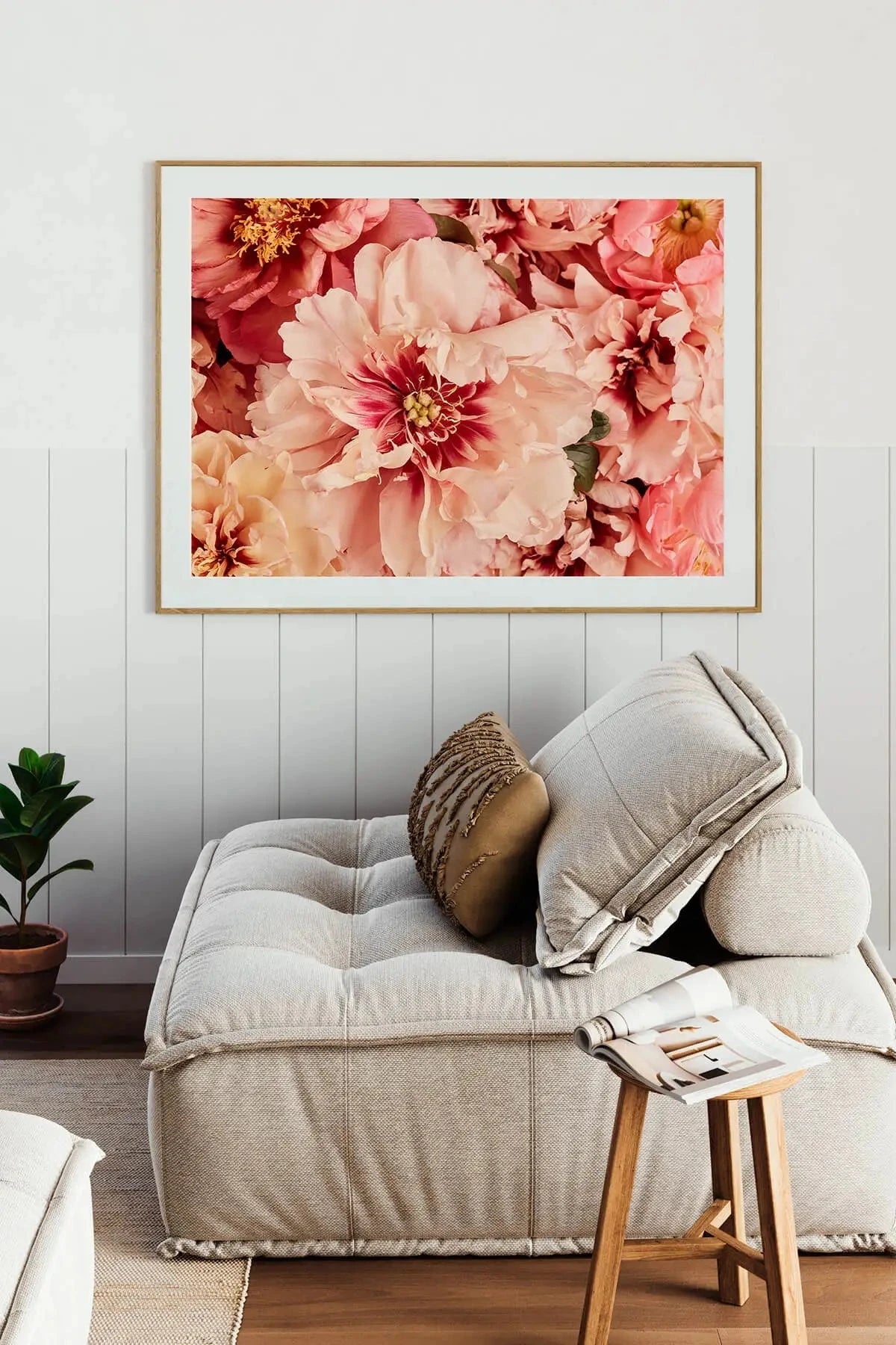 Fine art print of lush pink and coral peonies with golden stamens displayed above a neutral linen sofa in a coastal-style living room