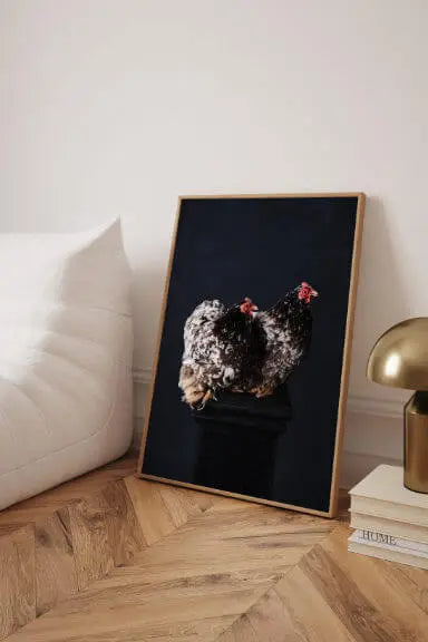 Fine art print of spotted guinea pig with pink flowers on black background, displayed in gold frame beside cream sofa and brass lamp on herringbone floor
